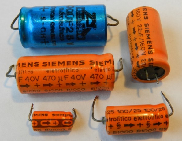 Figura 32 – Capacitores eletrolíticos úmidos da década de 1980, com indicação do polo positivo.