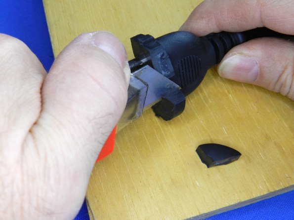 Figura 13 – Demonstração do corte do anteparo plástico. Note que as mãos estão afastadas da lâmina do estilete, que está sendo forçado para baixo, em direção à tábua. Neste caso, aplicando mais força foi possível cortar com o estilete o plástico rígido interno.